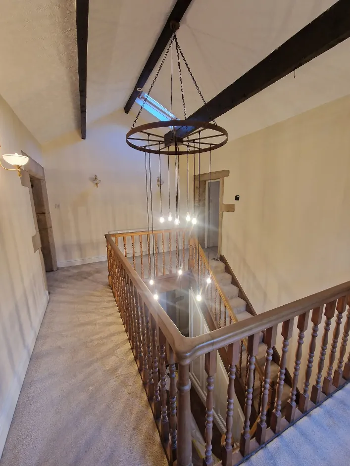 Vaulted barn conversion landing with cream walls, dark oak beams and a cartwheel chandelier