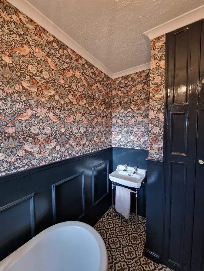 Bathroom with William Morris style bird wallpaper above dark navy wall panelling