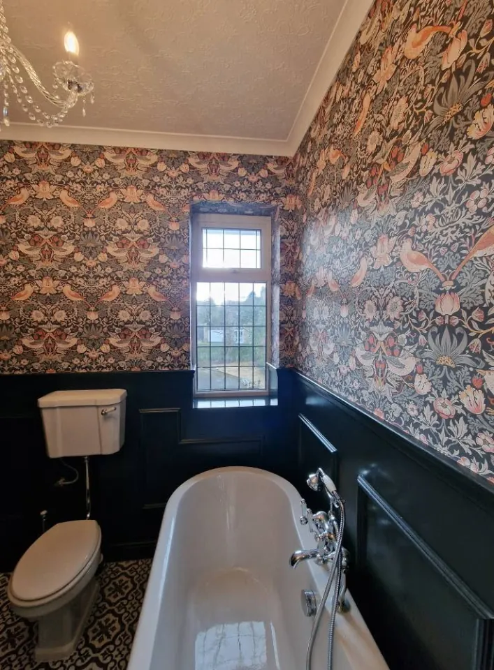Bathroom with patterned wallpaper, navy panelling and a roll top bath