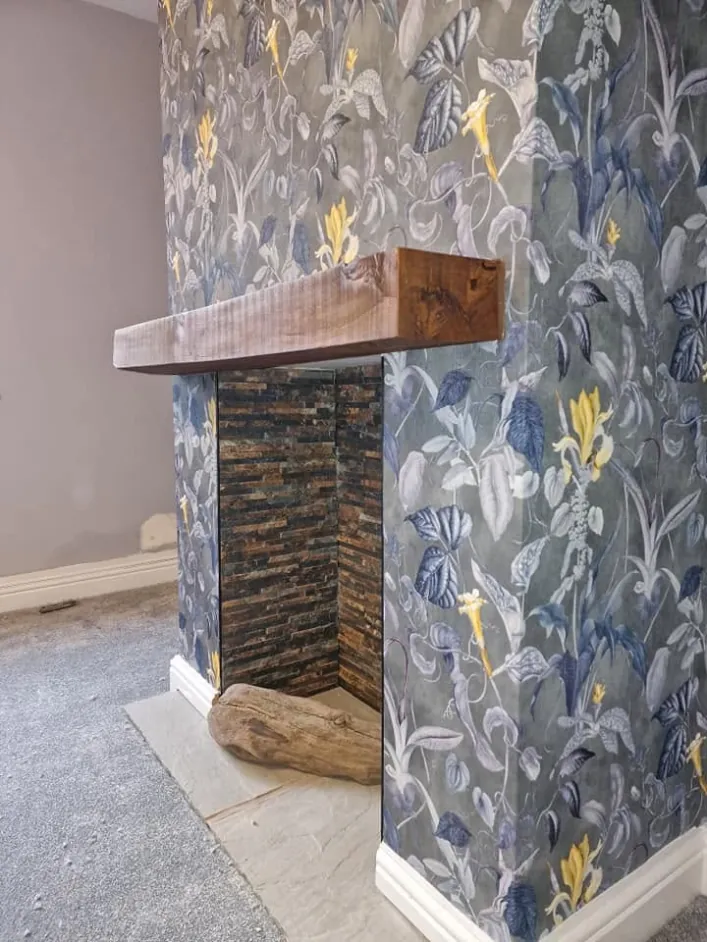 Chimney breast papered in a large blue and yellow floral print with an oak beam mantel