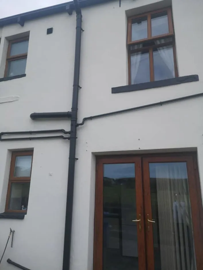 Rear of a stone house with smooth white masonry paint and black downpipes