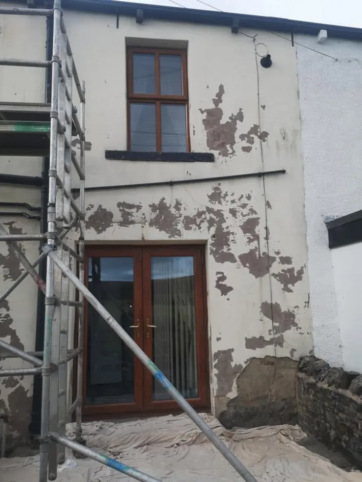 The same house before, with flaking paint and bare patches around the doors
