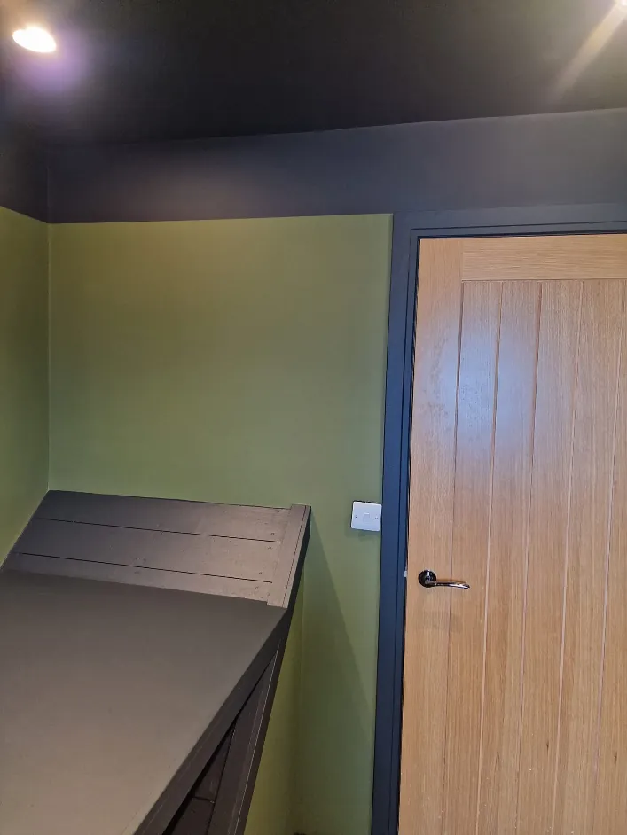 Small room in olive green with a navy ceiling, frames and built in seat