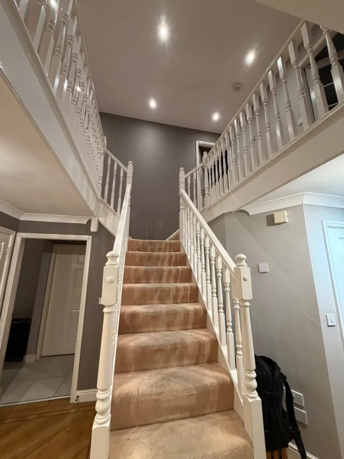 The same staircase before, with white spindles, grey walls and a worn carpet